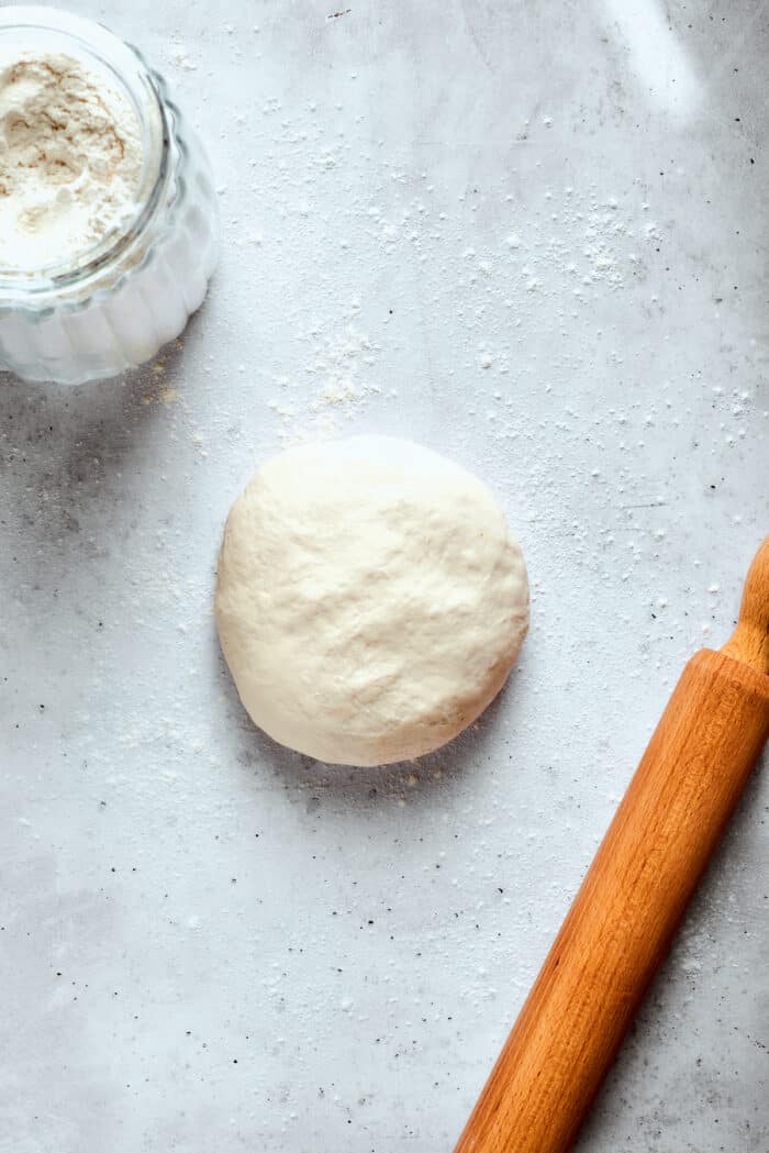 A ball of pizza dough is ready to be rolled with a rolling pin.