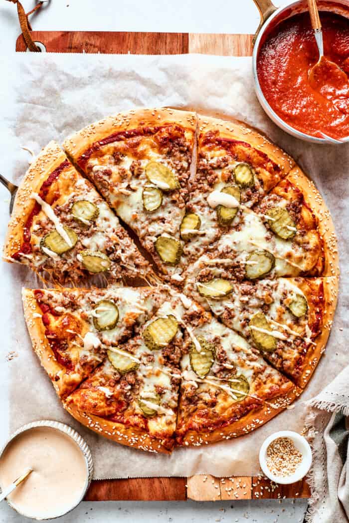 Bowls of sauce are arranged around a cheeseburger pizza.