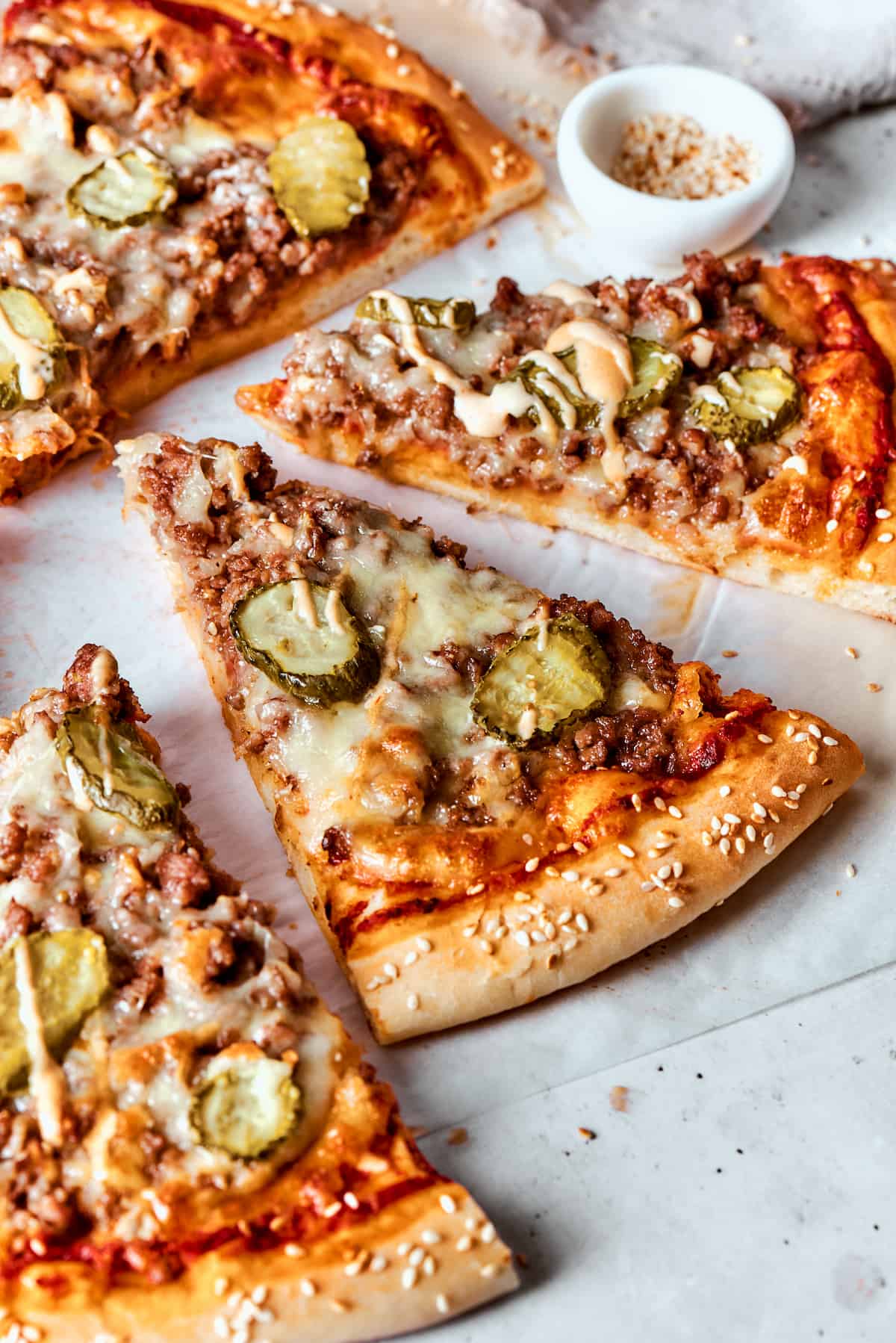 Cut slices of cheeseburger pizza topped with pickles.