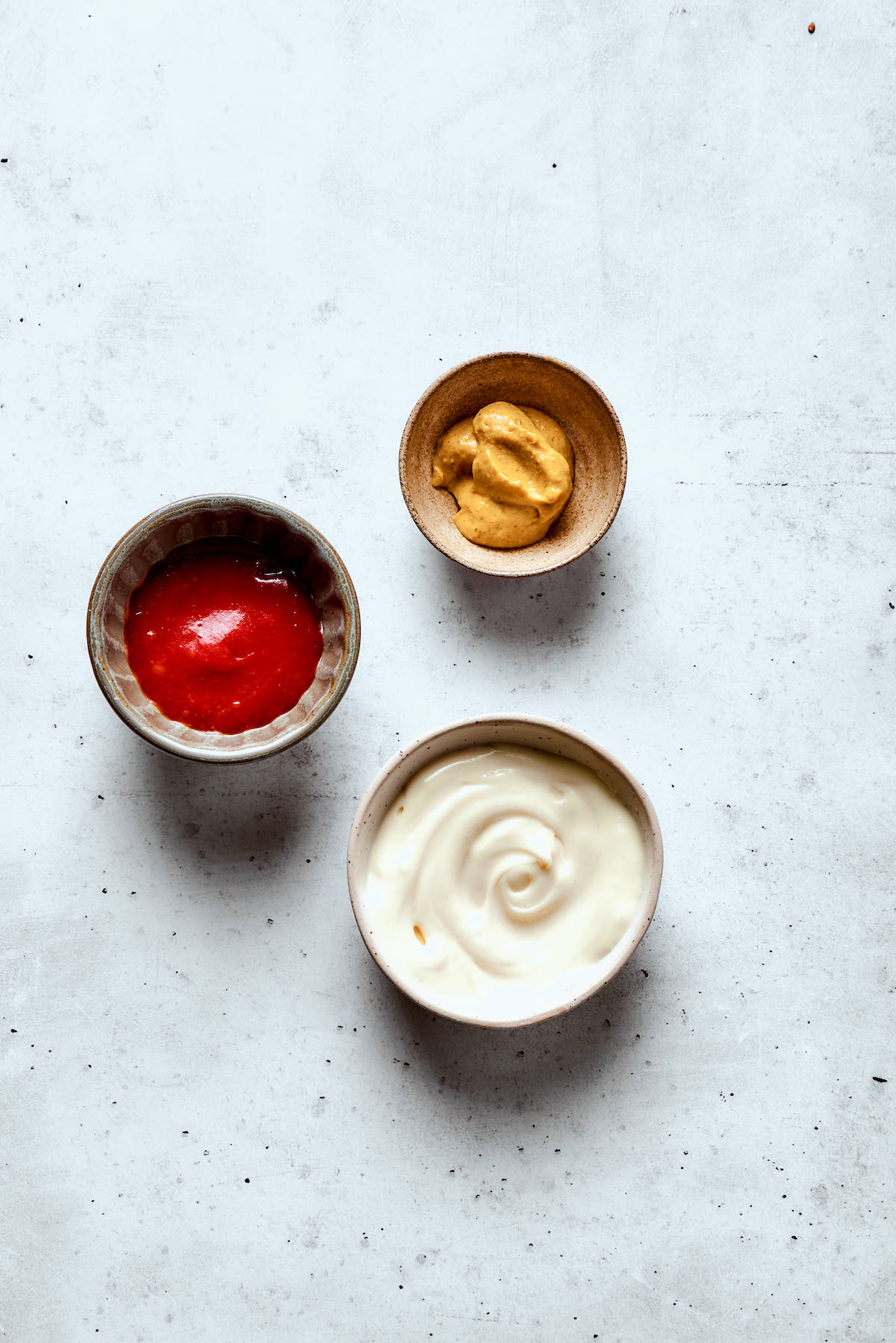 Ketchup, mustard, and mayonnaise portioned into little bowls.