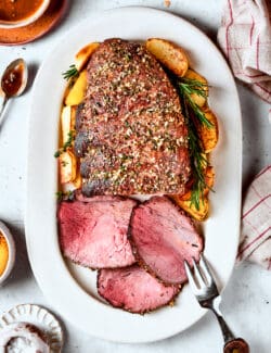 A white platter holds a sirloin tip roast with three slices cut from it.