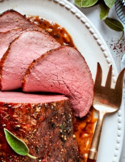 Slices of top round roast fan out from the roast on a platter.
