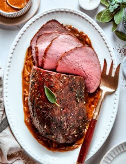 A white oval platter with a gold serving fork holds a cut top round roast.