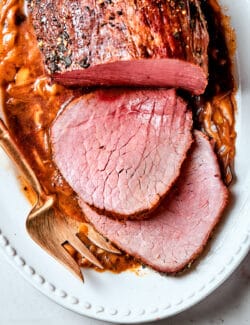 A platter holds a top round roast with slices next to it.