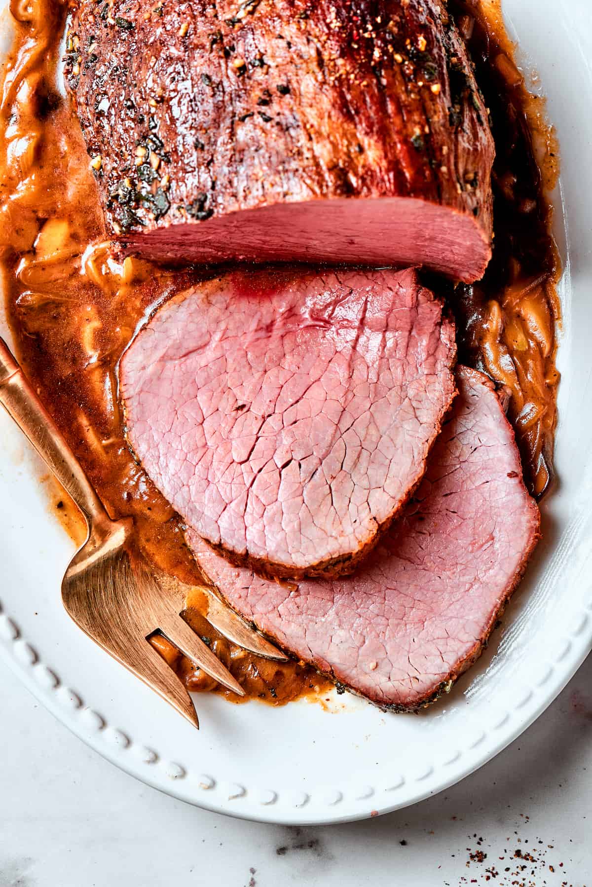 A platter holds a top round roast with slices next to it.