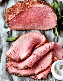 A pile of top round roast slices with the roast in the background.