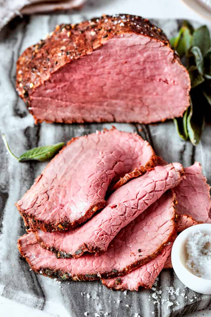 A pile of top round roast slices with the roast in the background.
