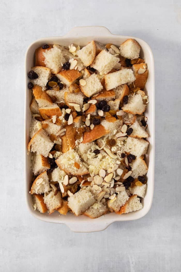 Shredded rolls, cheese, raisins, and almonds are combined in a baking dish.