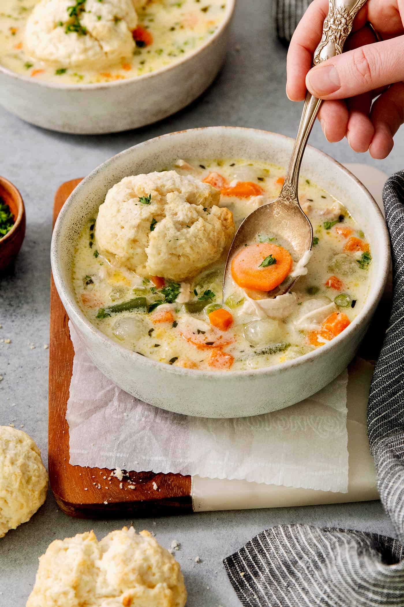 A hand holding a spoon lifts out a spoonful of chicken pot pie soup.