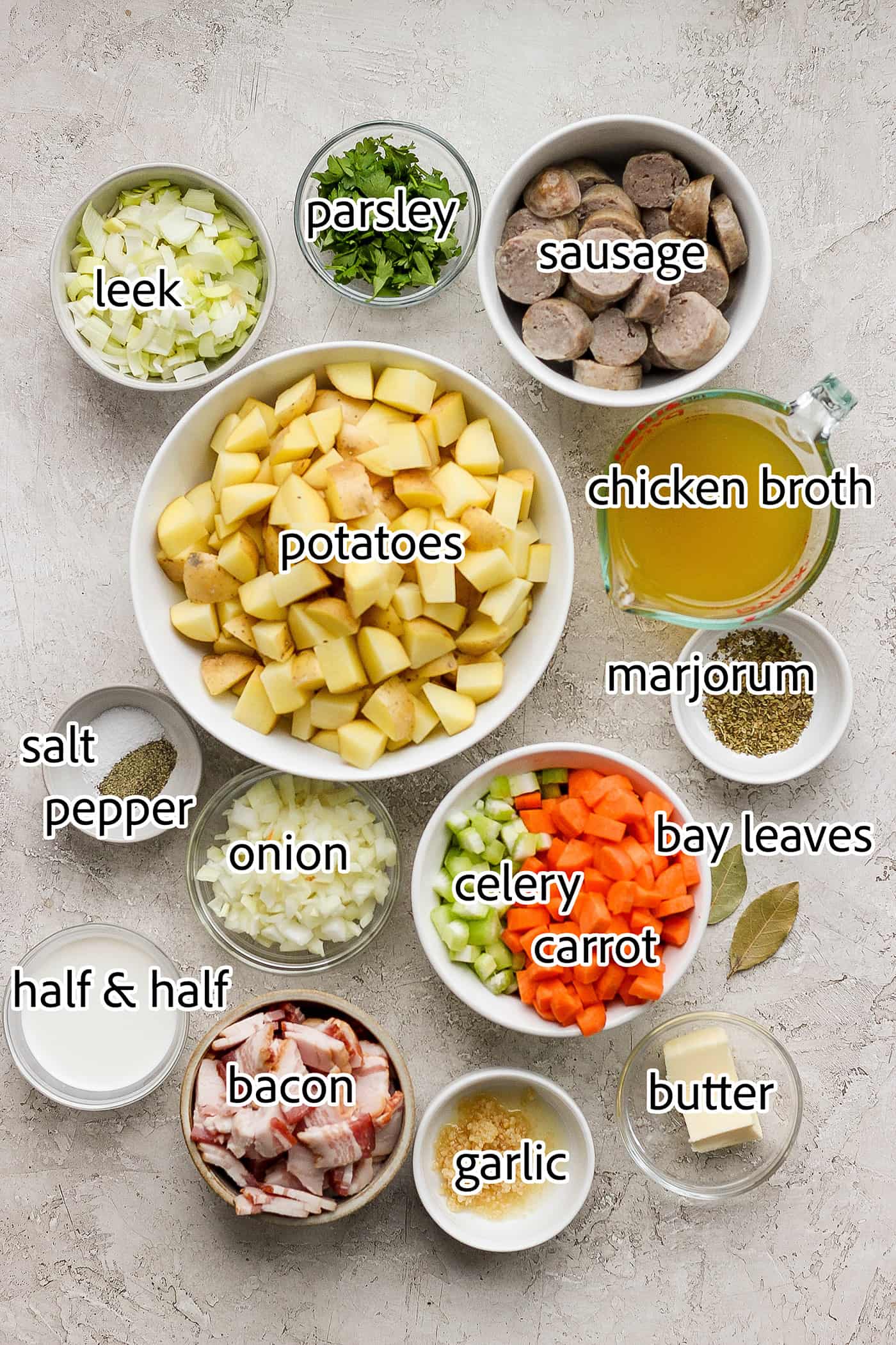 Ingredients needed to make German potato soup are shown: sausage, bacon, half and half, carrots, leek, onion, celery, chicken broth, bay leaf, parlsey.