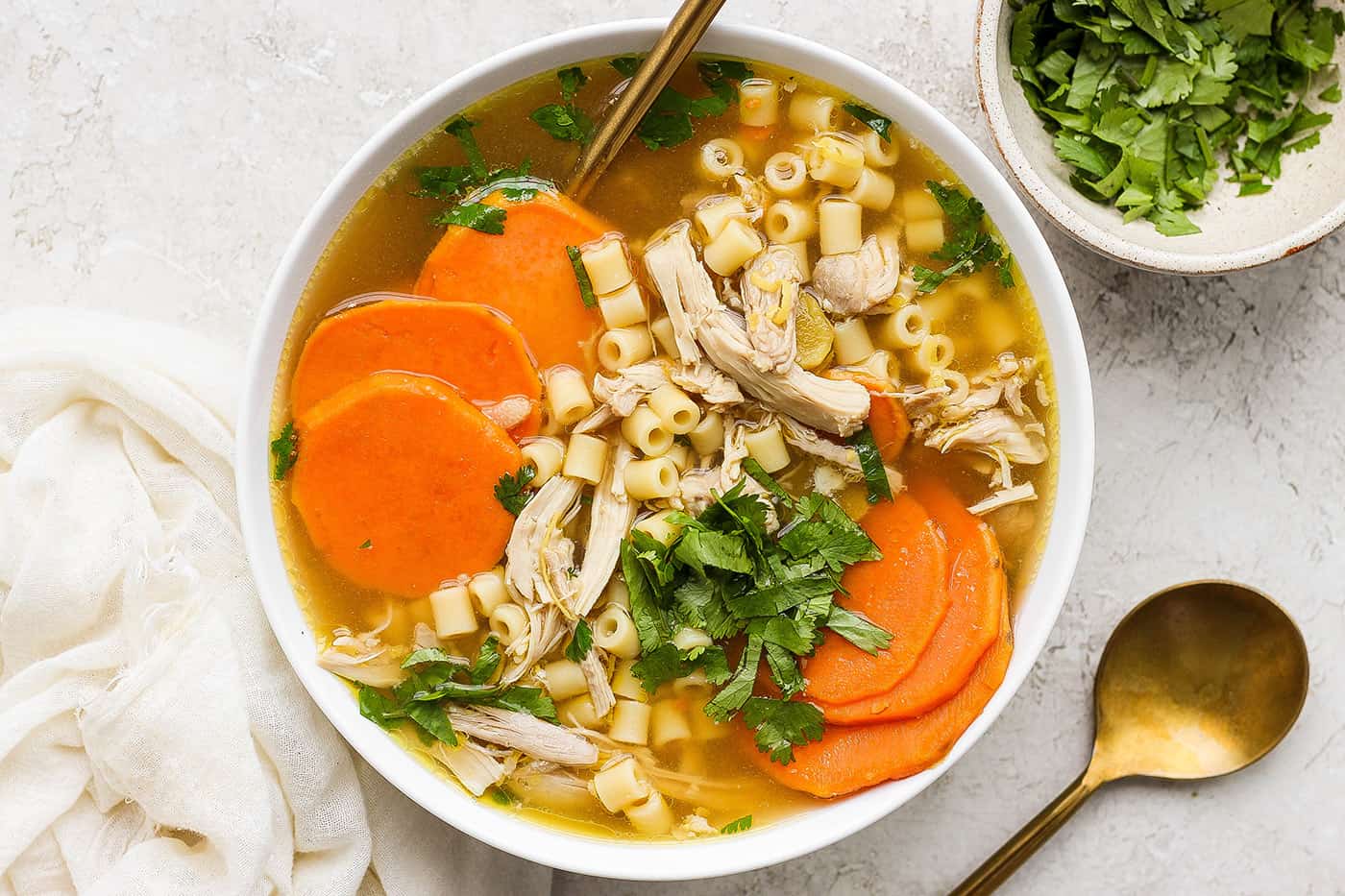 A hearty bowl of ginger chicken soup showing shredded chicken, sliced sweet potatoes, and pasta.