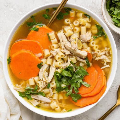 A hearty bowl of ginger chicken soup showing shredded chicken, sliced sweet potatoes, and pasta.