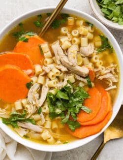 A hearty bowl of ginger chicken soup showing shredded chicken, sliced sweet potatoes, and pasta.