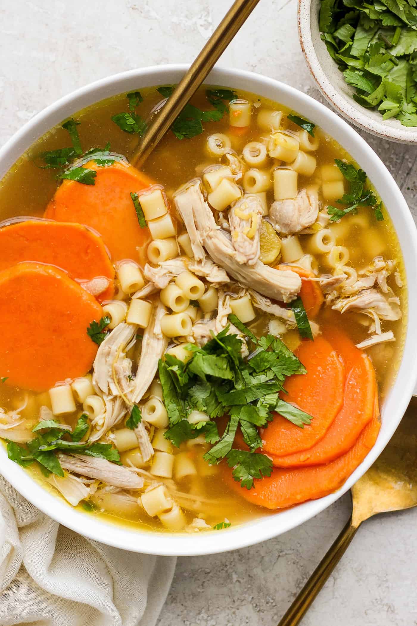 A hearty bowl of ginger chicken soup showing shredded chicken, sliced sweet potatoes, and pasta.