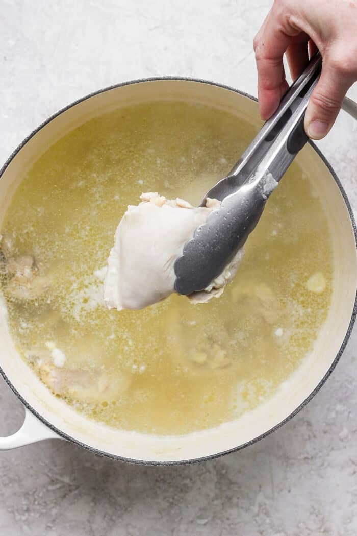 Tongs are used to remove the chicken from the broth.