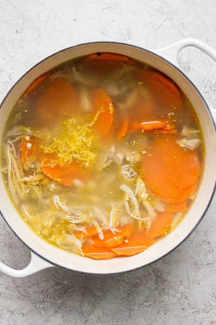 Sweet potato slices float on the top of a pot of ginger chicken soup.