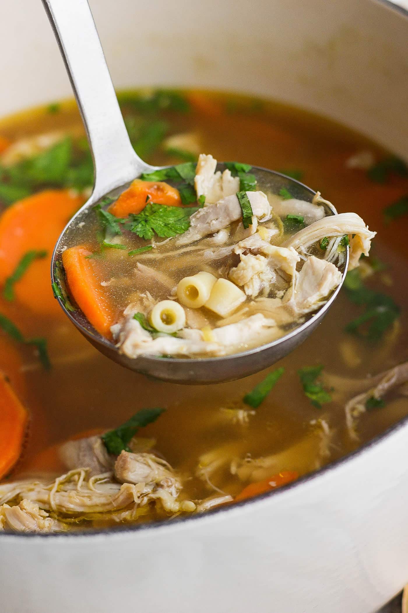 A ladleful of ginger chicken soup showing shredded chicken, pasta, and sweet potatoes.