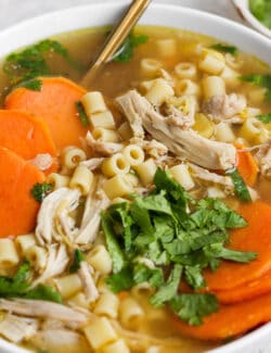 A bowl of ginger chicken soup topped with shredded chicken and sweet potatoes.