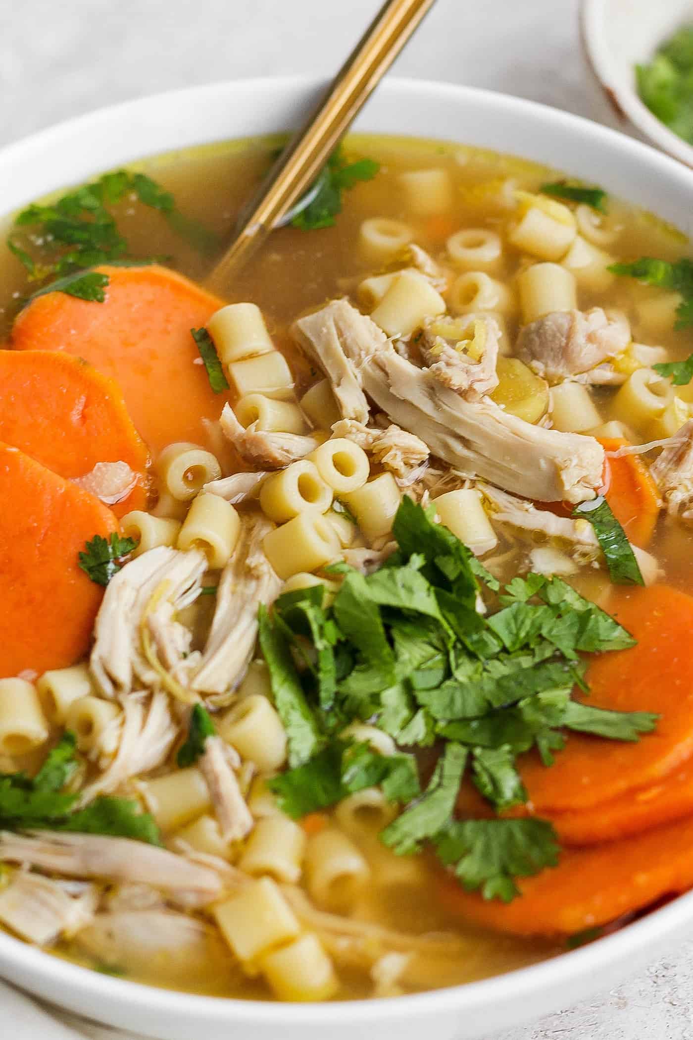 A bowl of ginger chicken soup topped with shredded chicken and sweet potatoes.