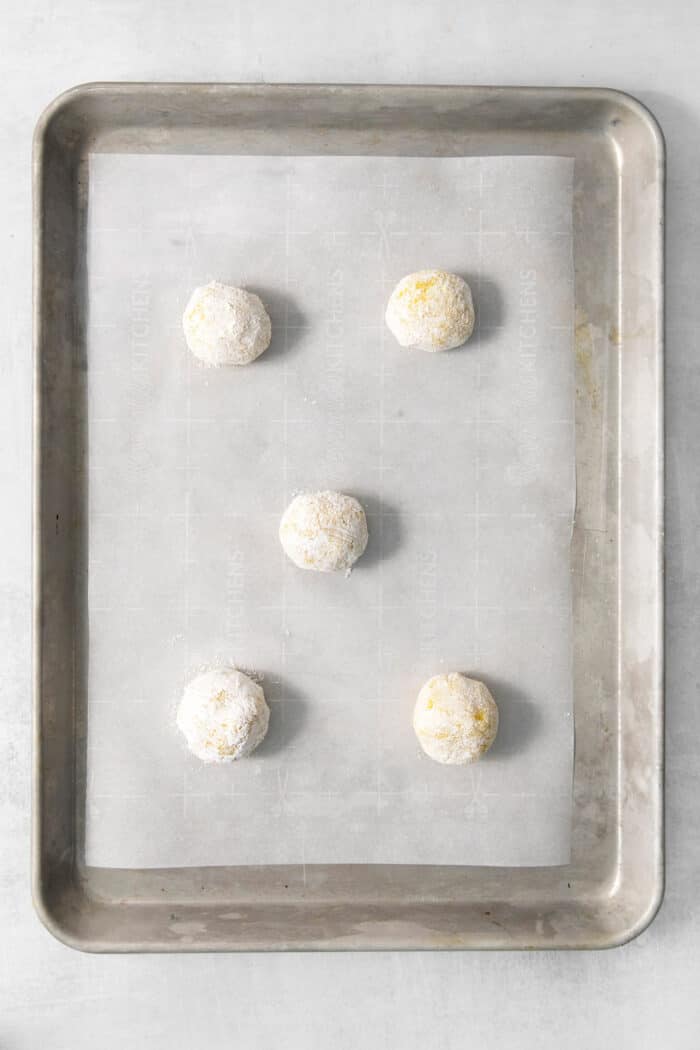 Lemon crinkle cookies are shown after being rolled in sugar on a baking pan.