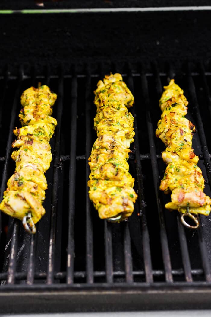 Chicken kabobs cook on a grill.