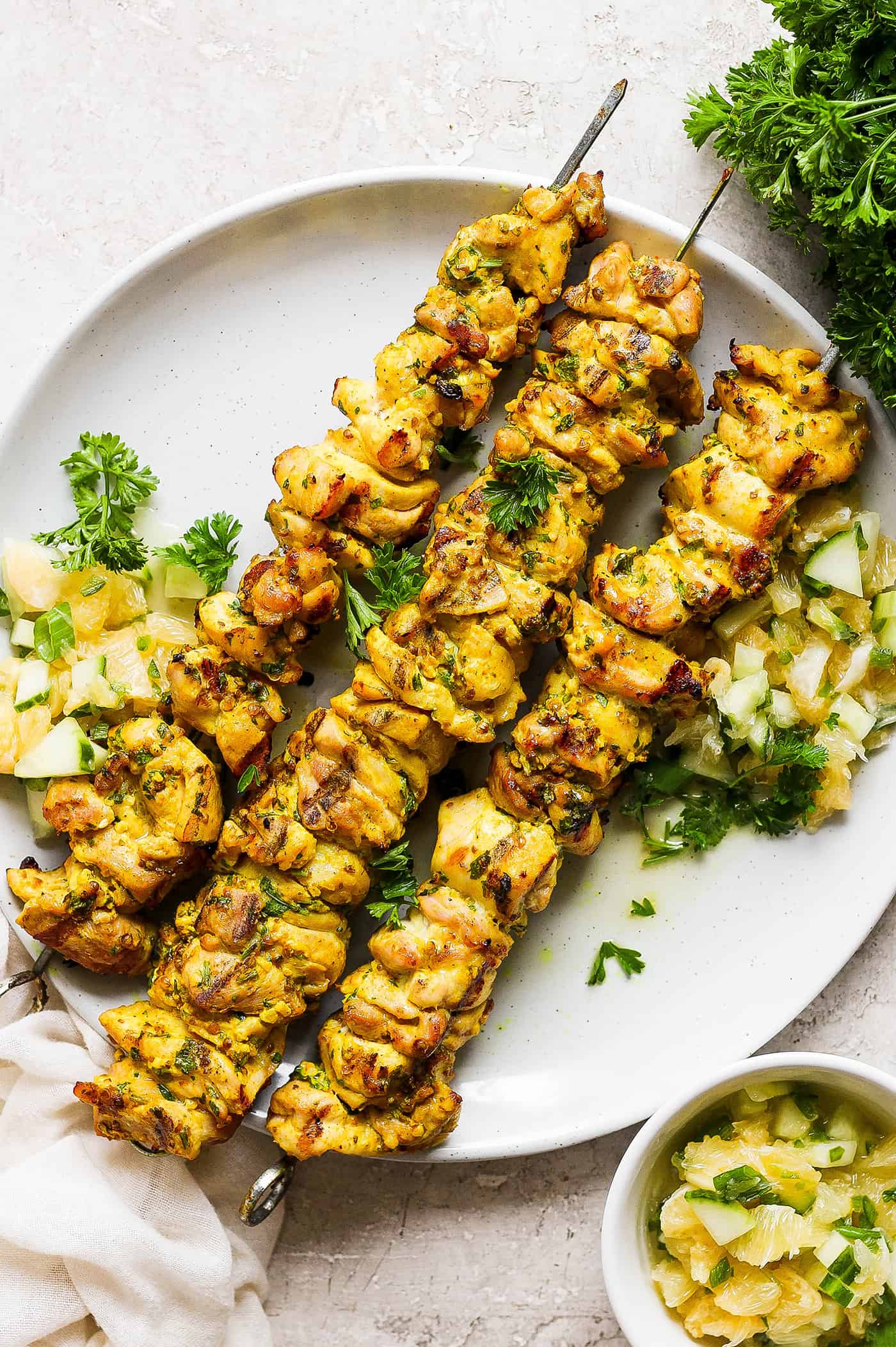 A plate holds three chicken kabobs with Meyer lemon salsa with more salsa in a bowl next to it.