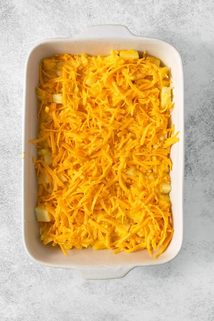 Shredded cheddar cheese tops the pineapple mixture in a white baking dish.