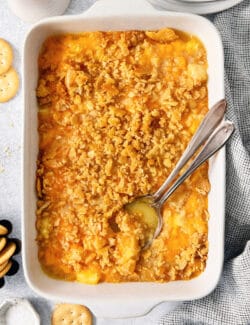 A serving spoon digs into a white baking dish holding pineapple casserole.
