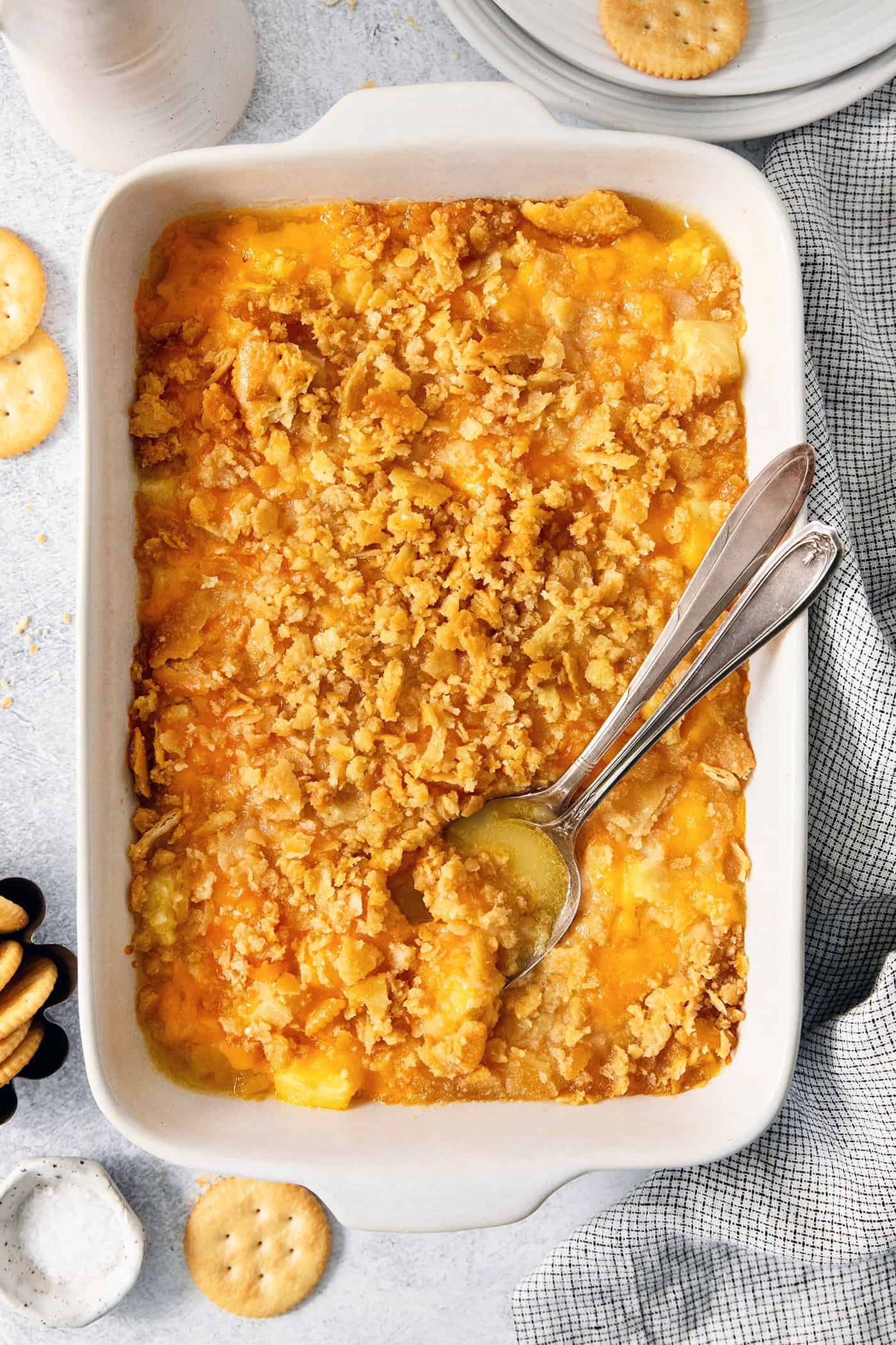 A serving spoon digs into a white baking dish holding pineapple casserole.