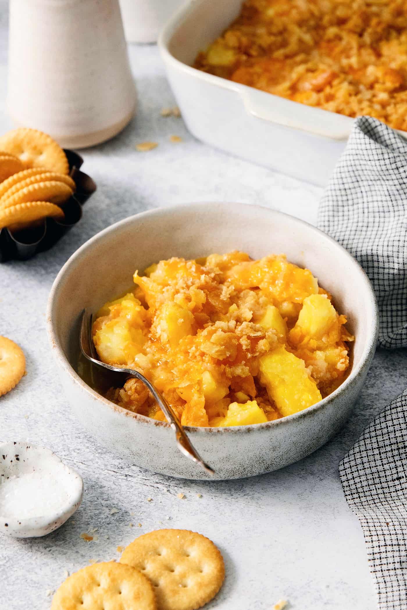 A white bowl holds a serving of pineapple casserole with a spoon.