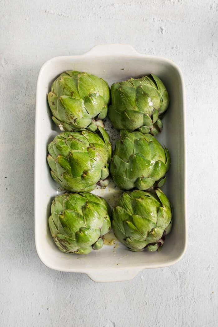 The six artichokes are placed in a baking dish.