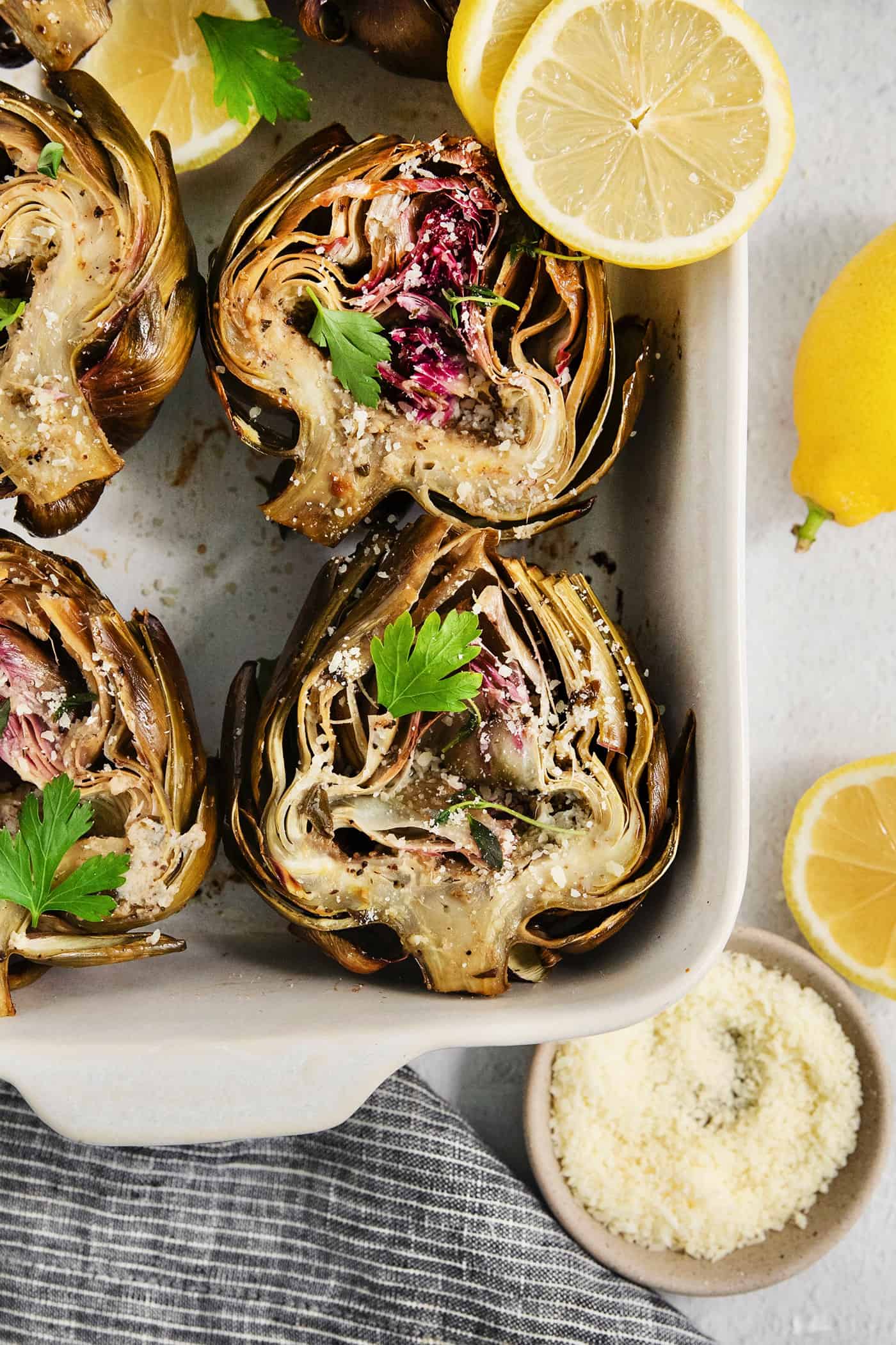 Roasted artichokes are shown close up garnished with parsley and surrounded by lemons.