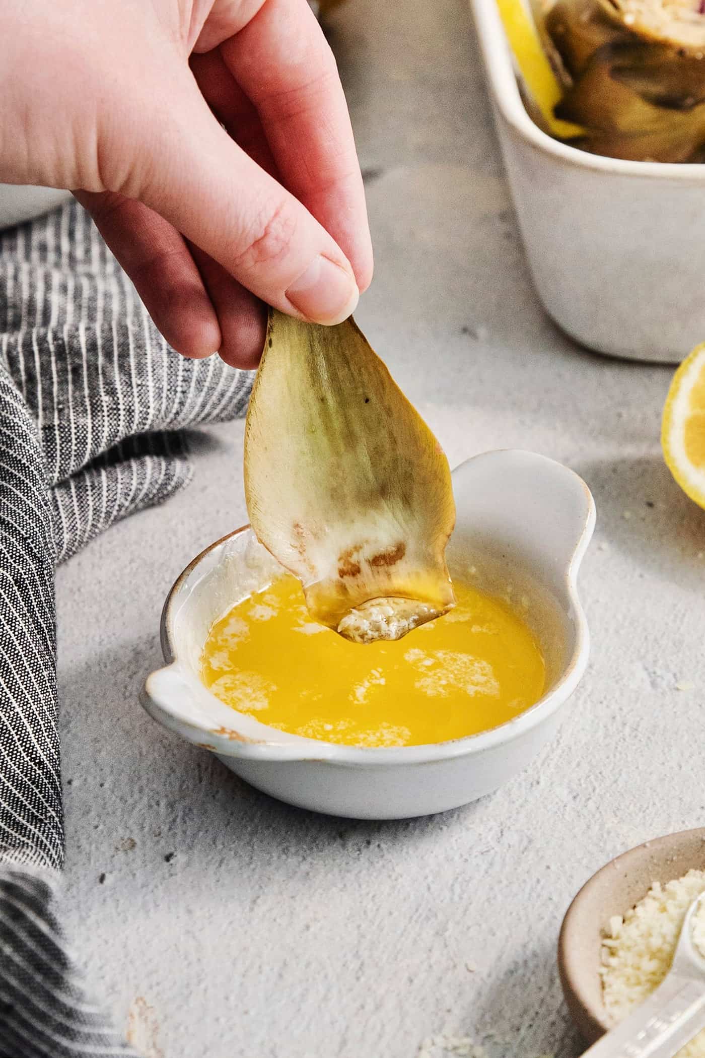 A hand dips an asparagus leaf into melted butter.