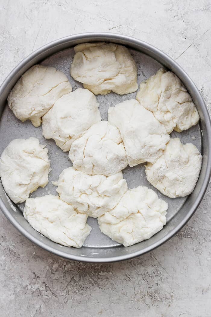 Touch of grace biscuit dough pieces are arranged in a metal baking round.