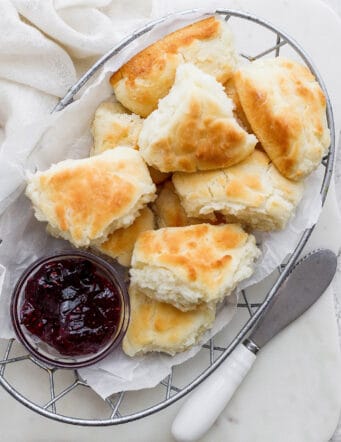 A wire basket holds browned touch of grace biscuits with a bowl of jam.