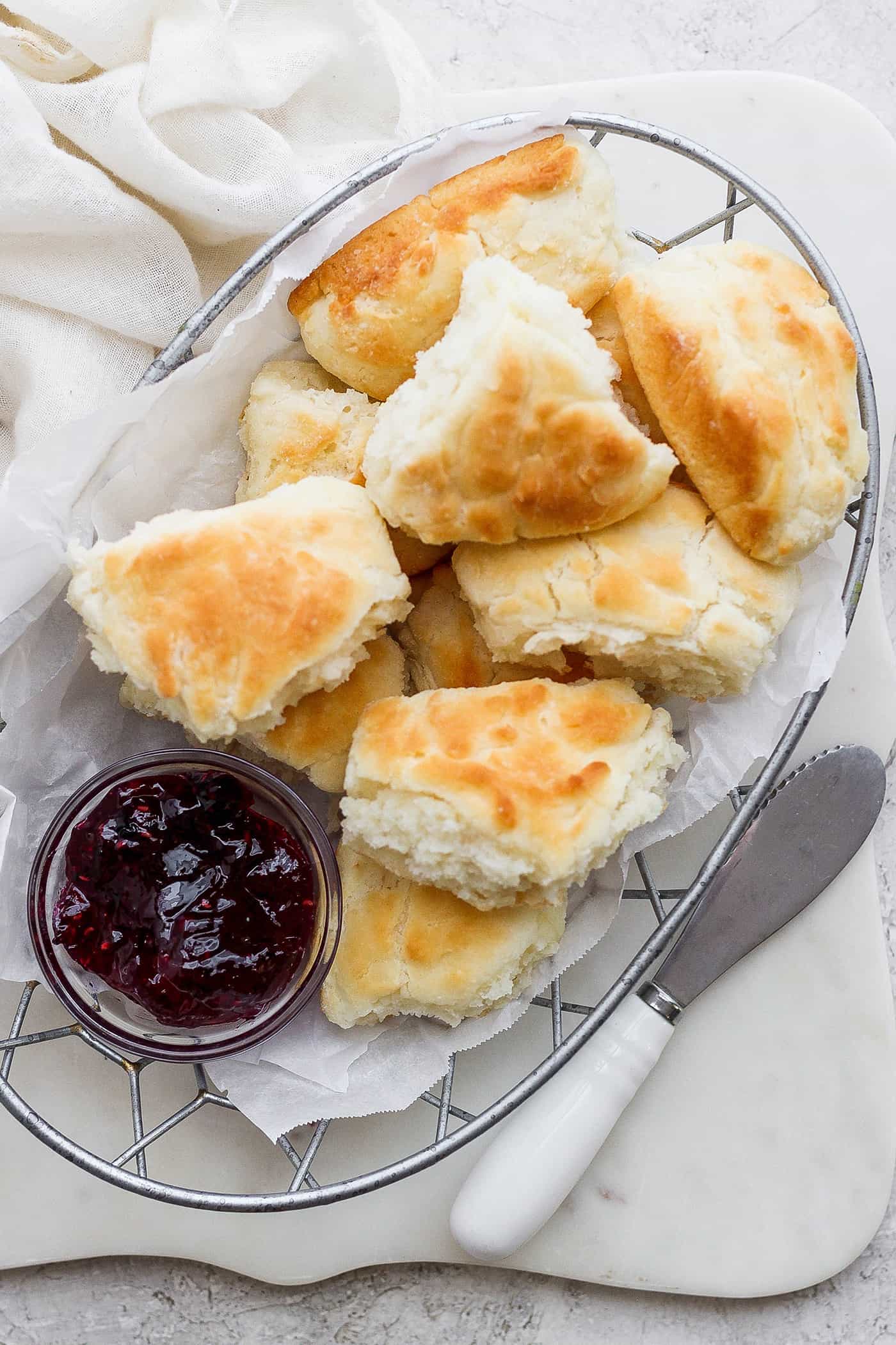 A wire basket holds browned touch of grace biscuits with a bowl of jam.