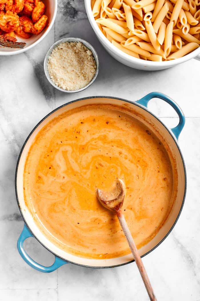 A spoon mixes a pot of sauce for cajun shrimp pasta.