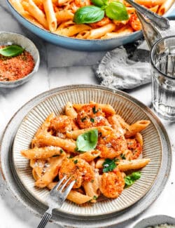 A serving bowl is full of cajun shrimp pasta with a portion served in a bowl nearby.
