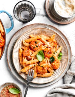 A tablescape shows a bowl of cajun shrimp pasta with a fork surrounded by bowls of seasoning.