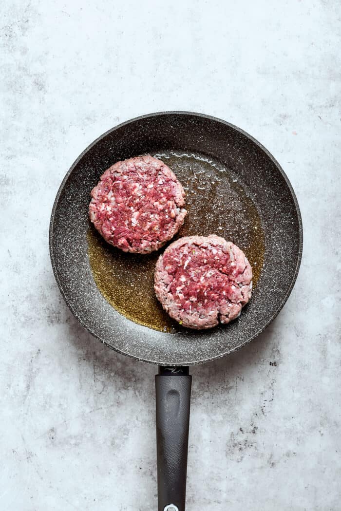 Blend two favorites to make this Pizza Burger recipe! Juicy beef patties are topped with tangy marinara, pepperoni, mozzarella & fresh basil. Two burger patties cook in a skillet.