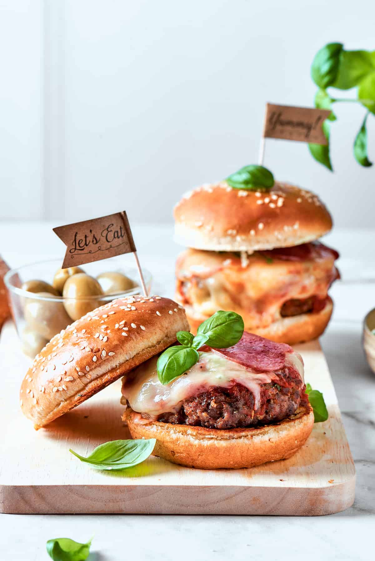 Blend two favorites to make this Pizza Burger recipe! Juicy beef patties are topped with tangy marinara, pepperoni, mozzarella & fresh basil. A flag tops pizza burgers topped with basil leaves