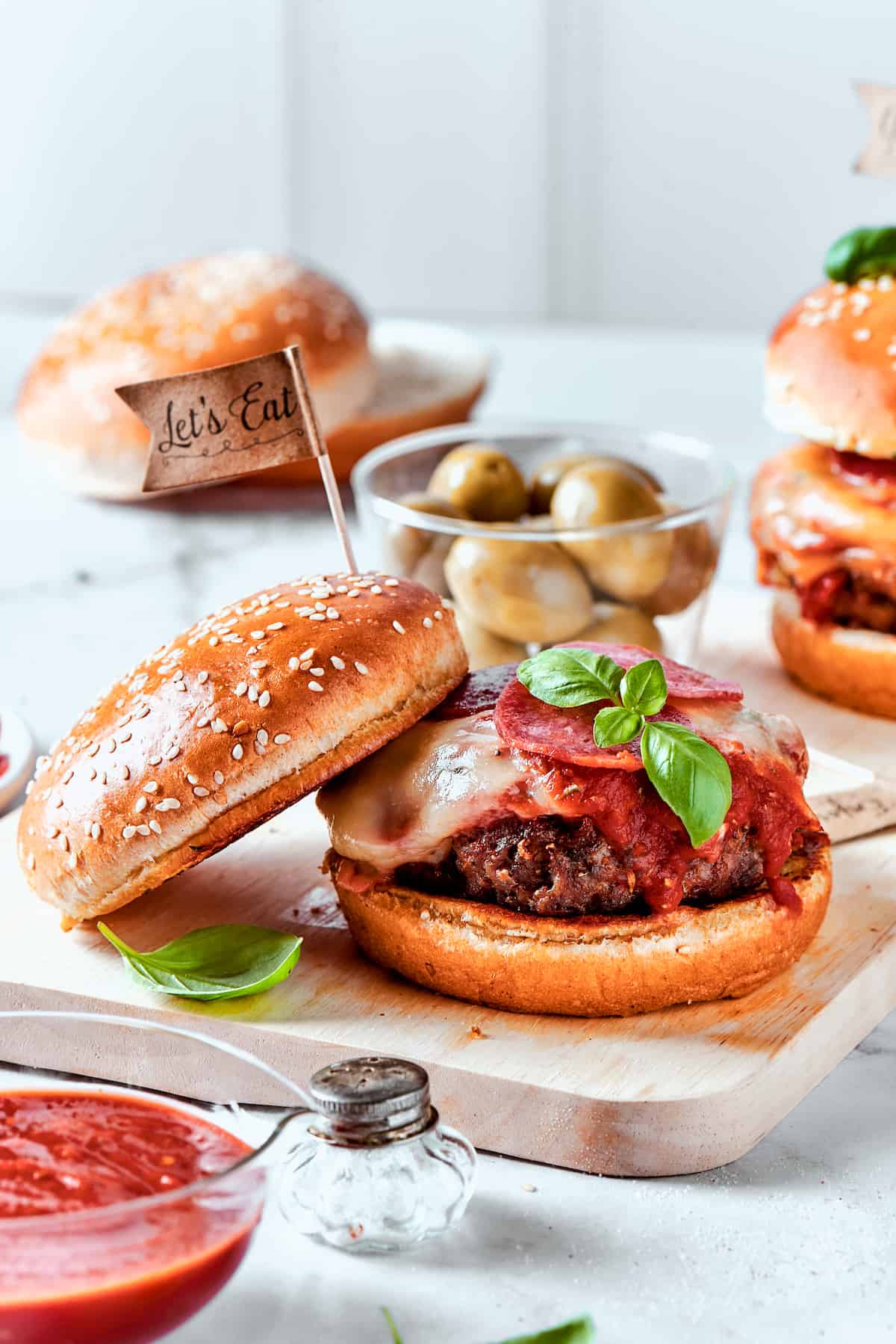 Blend two favorites to make this Pizza Burger recipe! Juicy beef patties are topped with tangy marinara, pepperoni, mozzarella & fresh basil. The top half of a bun rests to the side of a pizza burger.