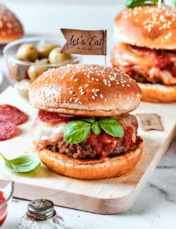 Pizza burgers are served on plates and garnished with basil leaves.