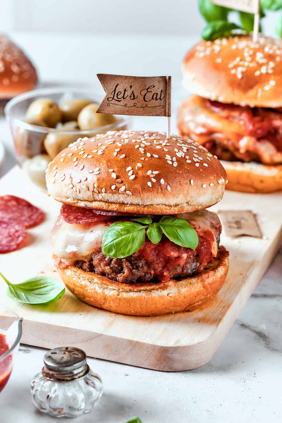Blend two favorites to make this Pizza Burger recipe! Juicy beef patties are topped with tangy marinara, pepperoni, mozzarella & fresh basil. Pizza burgers are served on plates and garnished with basil leaves.