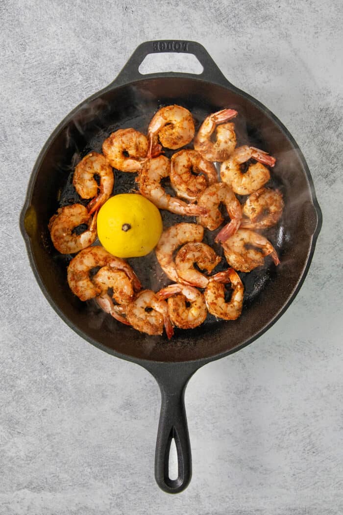 The shrimp are cooked in a skillet with a lemon.