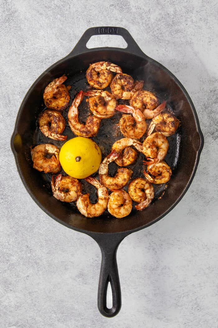 The shrimp are fully cooked in the skillet with a lemon.