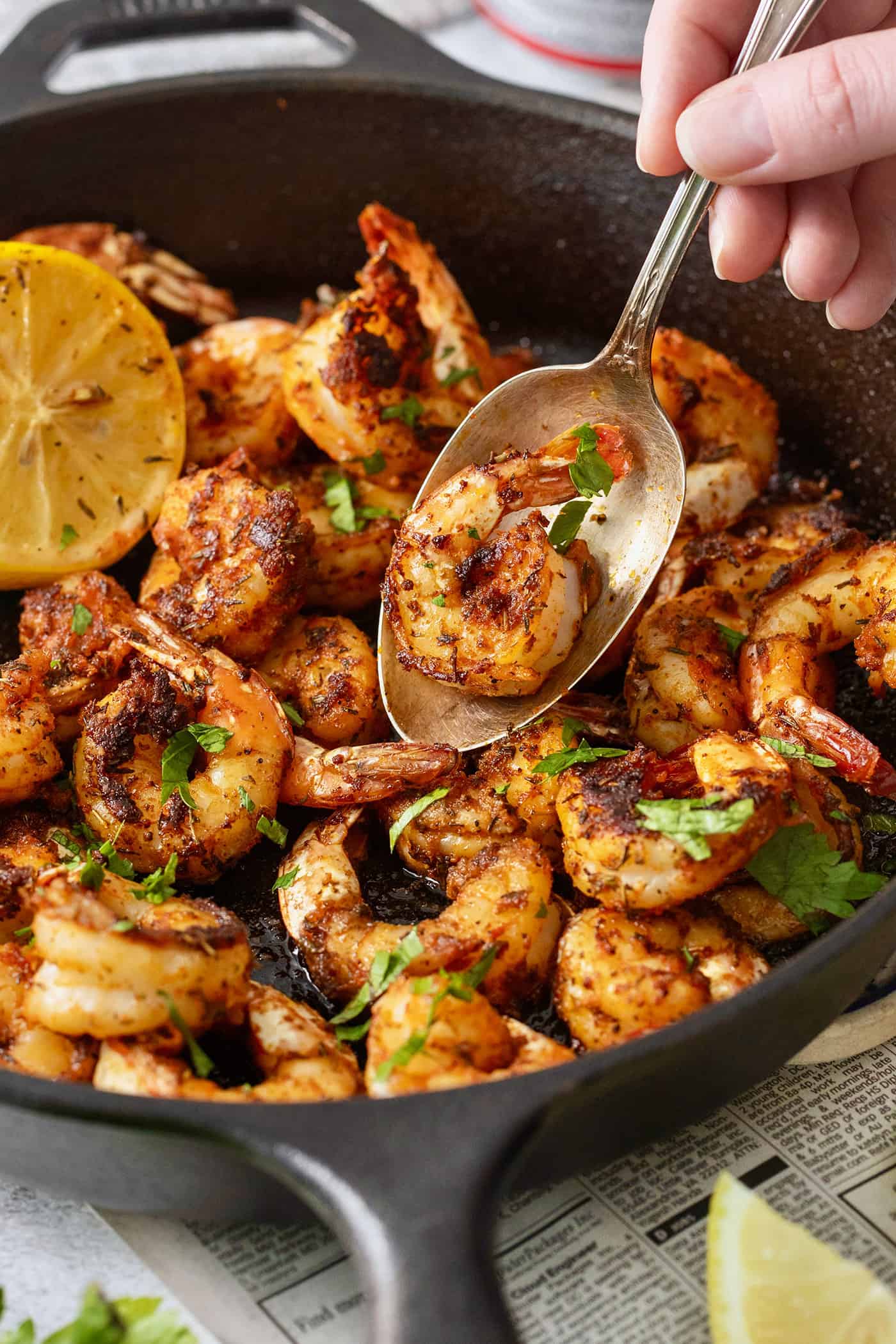 A spoon lifts out a piece of blackened shrimp from a skillet of shrimp.