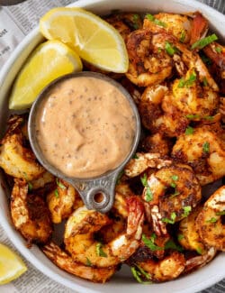 A bowl of blackened shrimp is served with shrimp dipping sauce and lemon wedges.