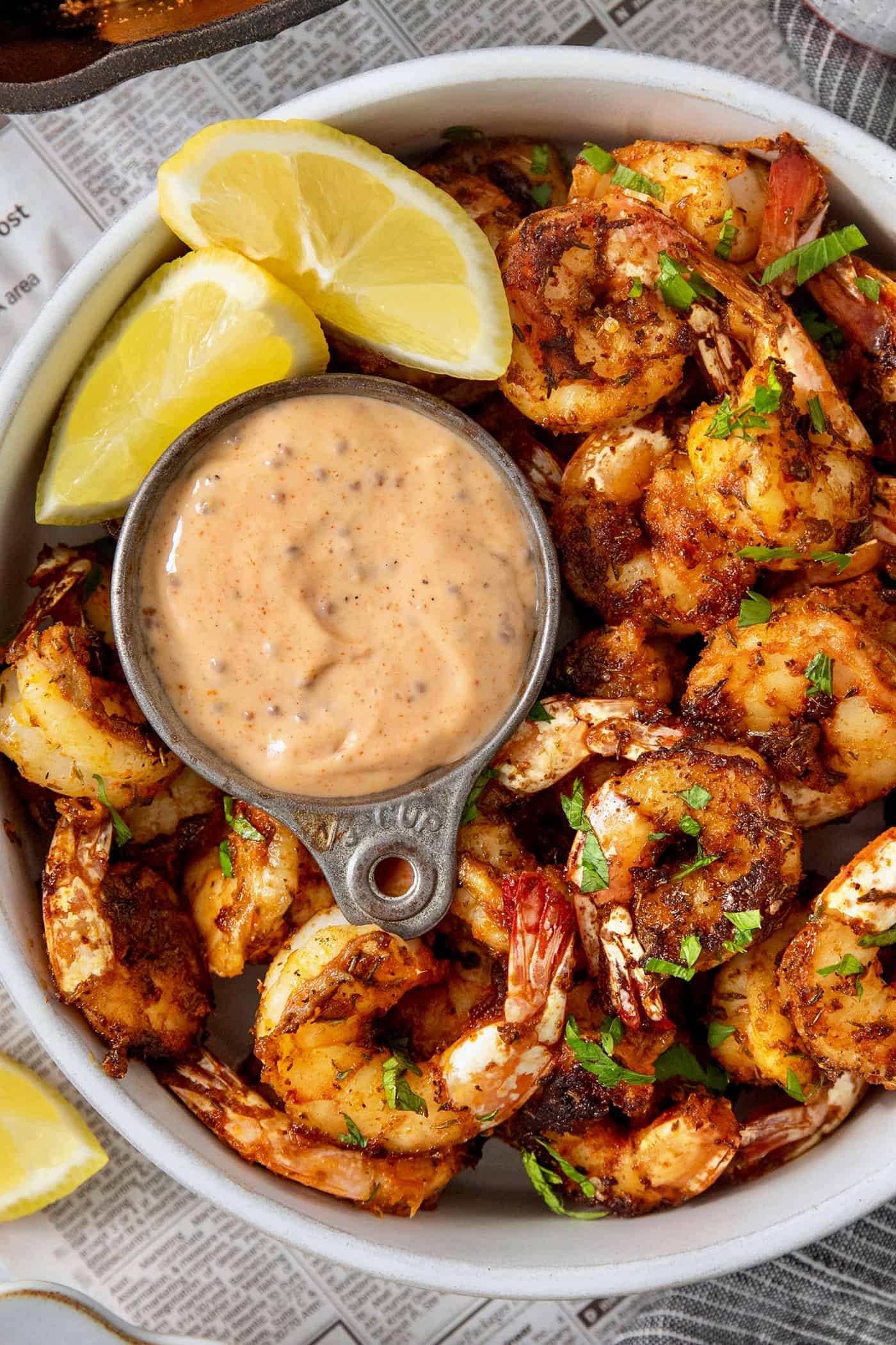 A bowl of blackened shrimp is served with shrimp dipping sauce and lemon wedges.