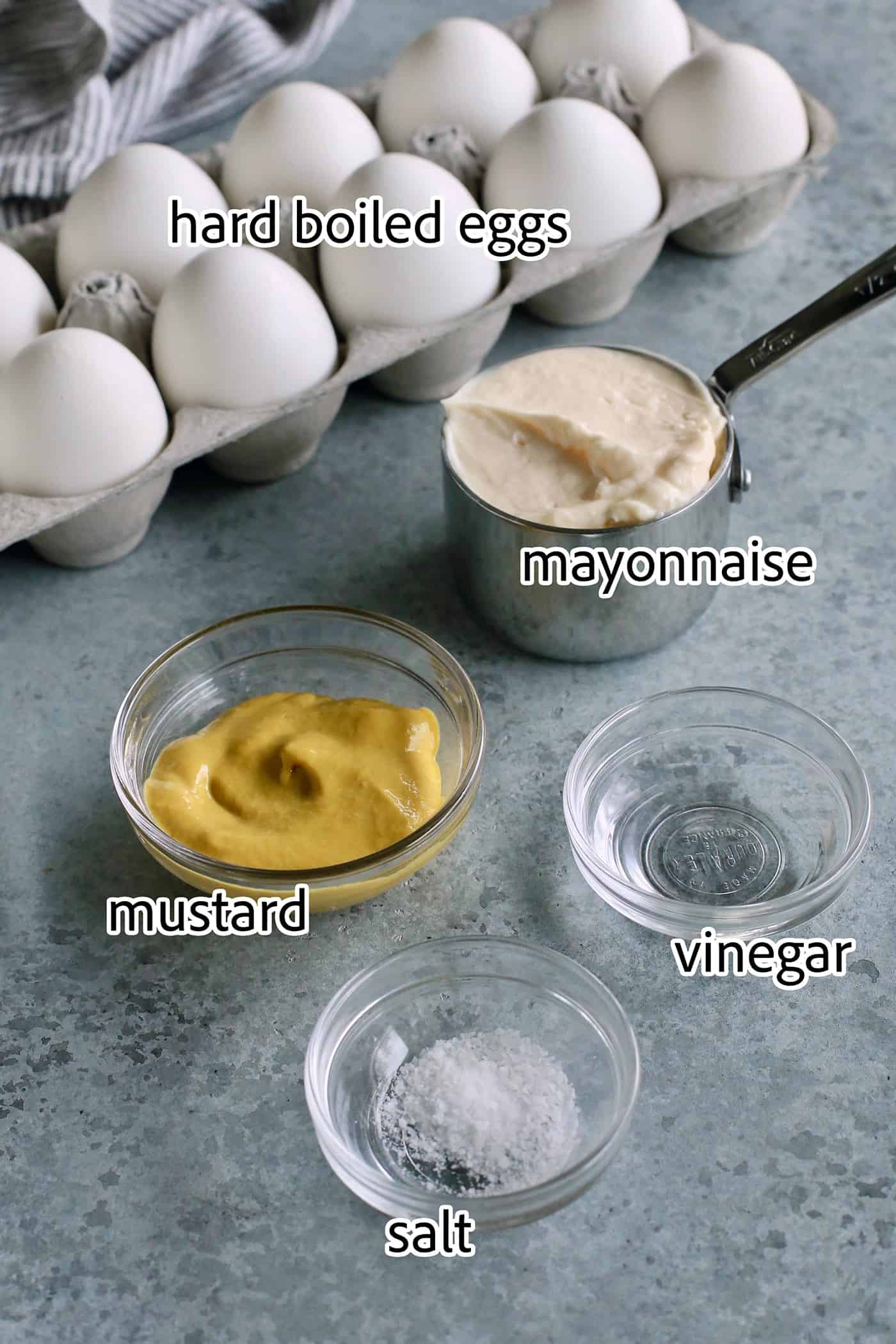 Ingredients for classic deviled eggs are shown: hard boiled eggs, mustard, mayonnaise, vinegar, salt.